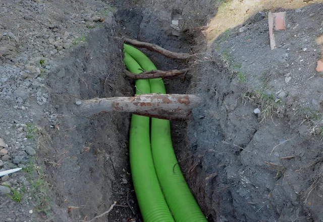 A bunch of green pipes are laying in the dirt